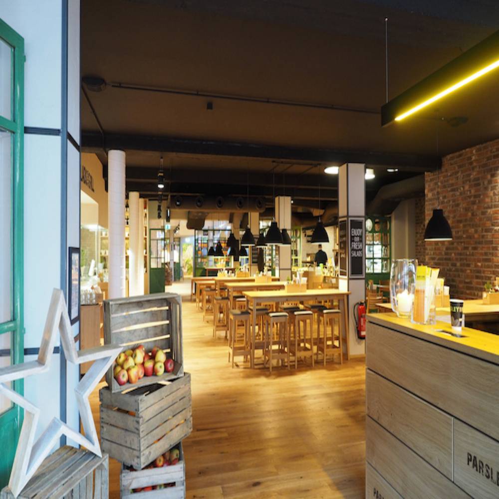 Innenansicht eines Restaurants mit Tischen und Stühlen, beleuchtet durch LED-Hallenstrahler im Retro-Design, die eine warme Atmosphäre erzeugen.