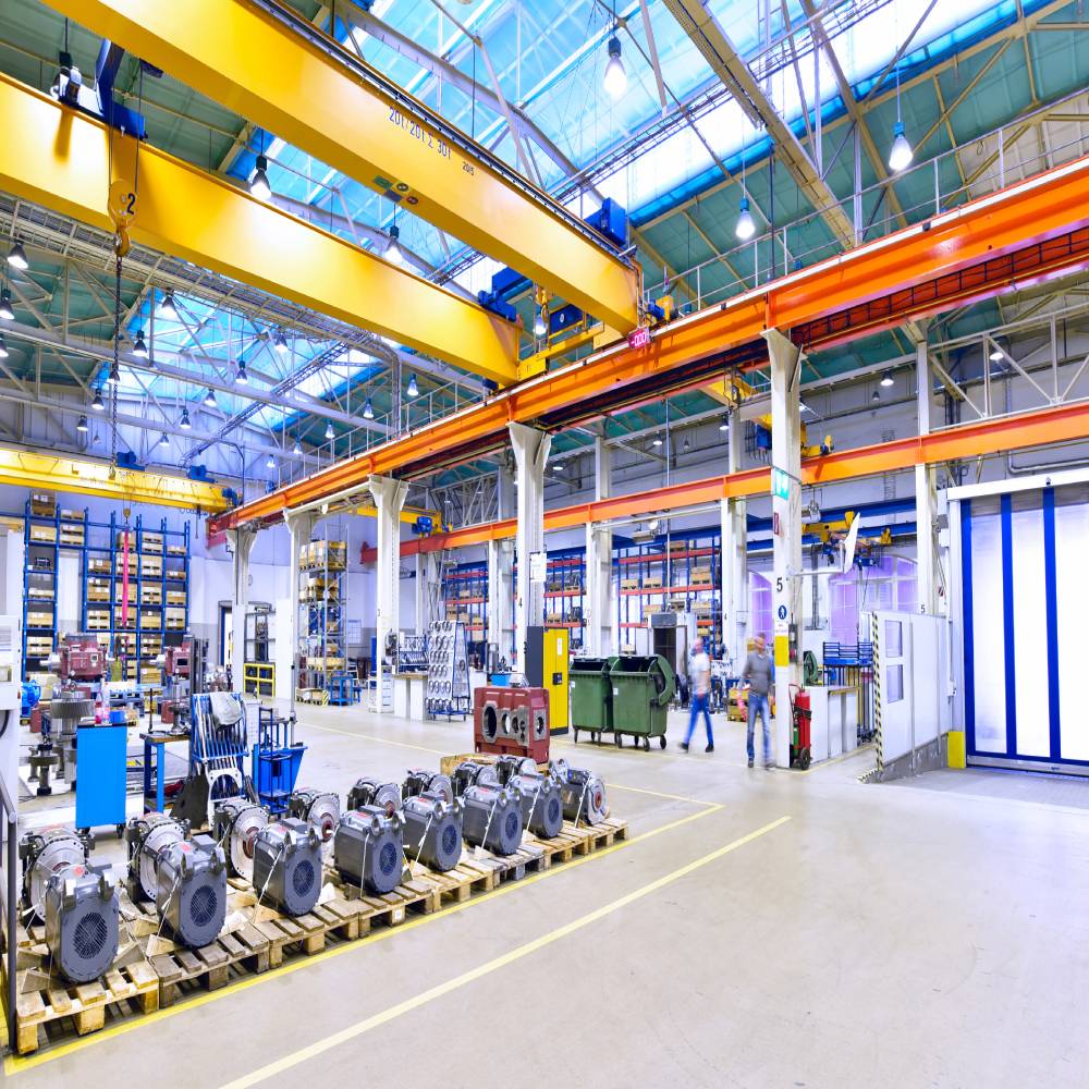 Helle Industriehalle mit Maschinen und geordneten Arbeitsplätzen, die gleichmäßig ausgeleuchtet ist durch moderne LED-Hallenstrahler.