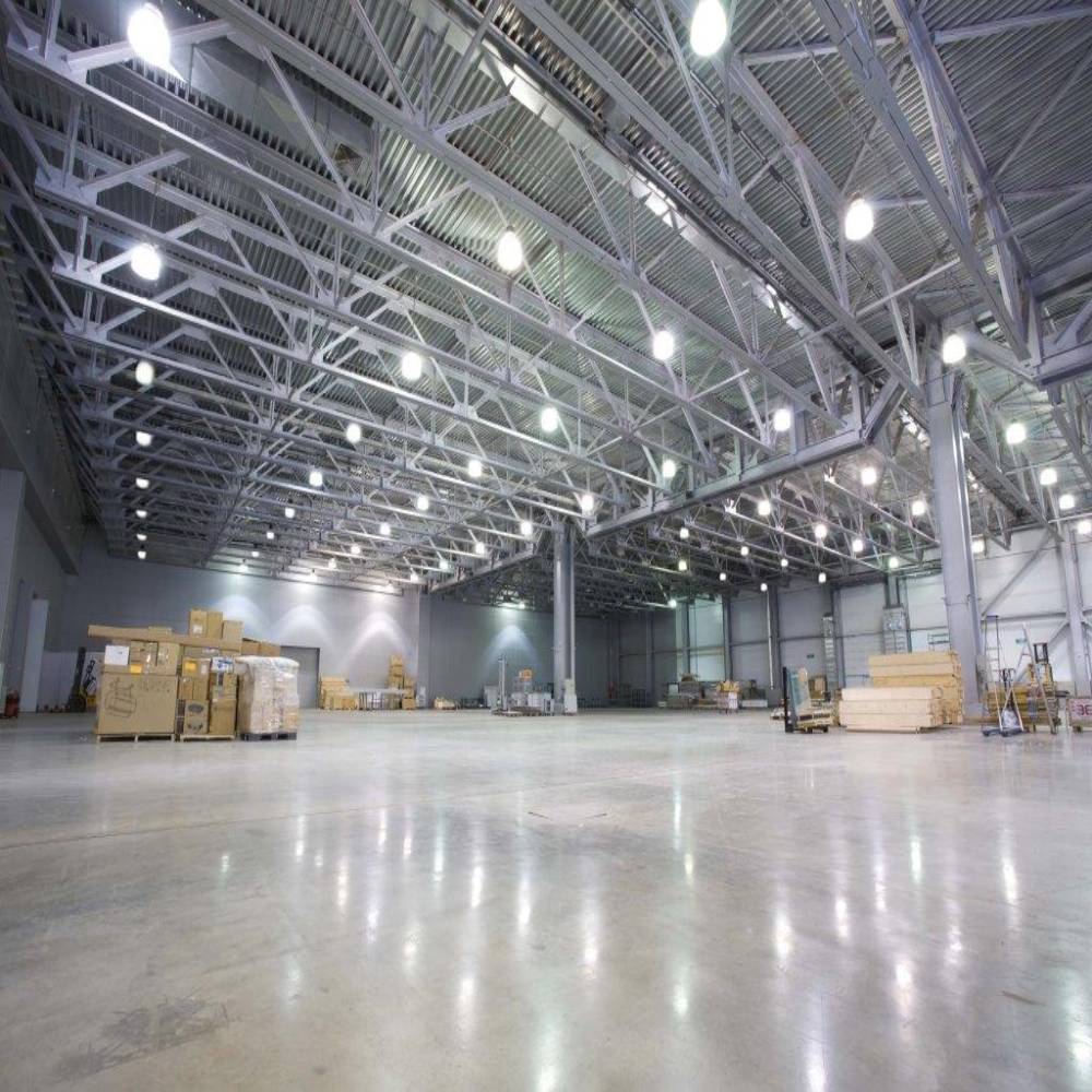 Weitläufige, leere Industriehalle mit glänzendem Betonboden, perfekt ausgeleuchtet durch gleichmäßig verteilte LED-Hallenstrahler.