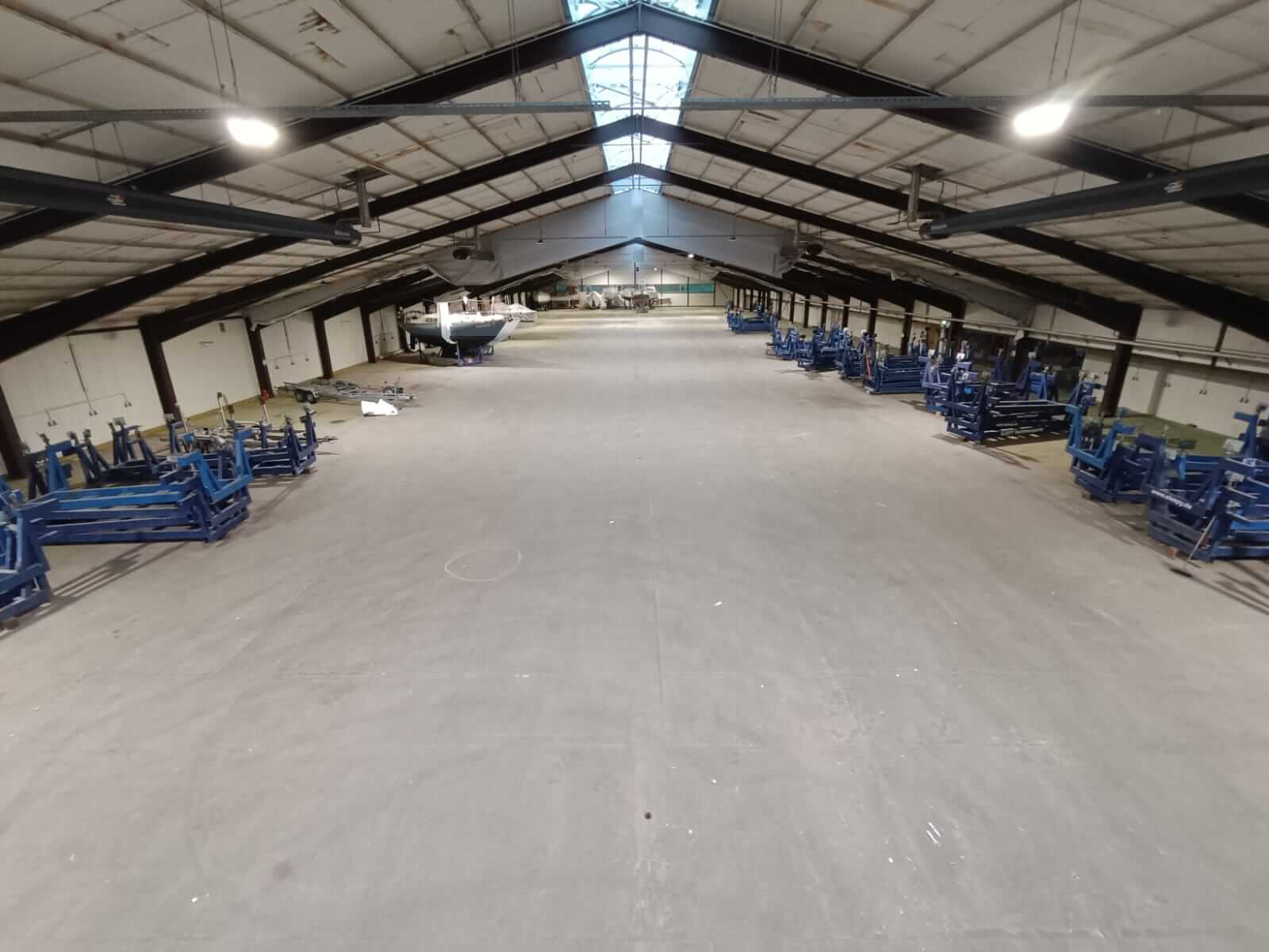 Referenz Sporthafen Kiel 2 Weitwinkelaufnahme der hell beleuchteten Lagerhalle am Sporthafen Kiel, mit Lagergestellen und einem gelagerten Boot im Hintergrund.