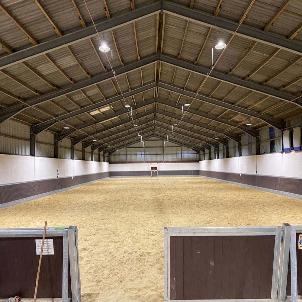 ÜInnenansicht einer Reithalle mit Sandboden, die durch LED Hallenstrahler blendfrei und gleichmäßig für den Pferdesport ausgeleuchtet wird.
