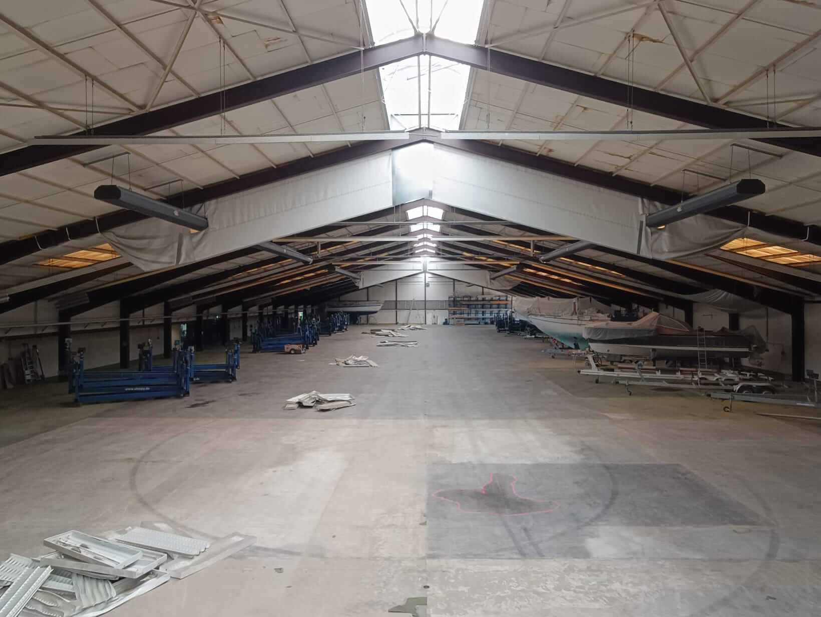 Referenz Sporthafen Kiel 5 Weite Aufnahme der leeren Lagerhalle am Sporthafen Kiel, die das natürliche Licht durch die Oberlichter und die Umgebung vor der endgültigen LED-Installation zeigt.